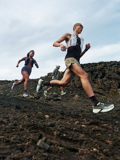 Trail runners navigating a rugged, rocky mountain path under cloudy skies